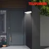 An outdoor wall lamp illuminates a modern gray door and a potted plant. Produktbild-Vorschau