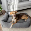 A dog is lying in a dog bed next to a sofa. Produktbild-Vorschau