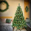 A Christmas tree with warm lights is set up in a bedroom next to a bed with festive pillows. Produktbild-Vorschau