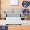 A white electric heater is placed on a fluffy rug in front of a gray sofa in a living room. There are marketing graphics in the upper right and lower left corners. Náhľad obrázku produktu