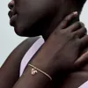 Close-up of a person's arm wearing a gold bracelet with a monstera leaf charm. Podgląd zdjęcia produktu