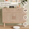 A light wood sideboard with slatted doors and drawers, shown in a room setting with decorative items and a robot vacuum cleaner on the floor. Podgląd zdjęcia produktu