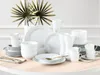 A collection of white ceramic dinnerware and mugs arranged on a light-colored table. Produktbild-Vorschau