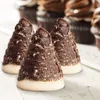 Three chocolate-covered cone-shaped pastries with a tan cookie base, arranged on a white wooden surface. Several chocolate cupcakes are visible in the blurred background. Produktbild-Vorschau