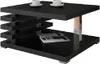A modern black coffee table with a unique tiered design and a silver accent leg, shown with two white coffee cups and a magazine on the lower shelf. Náhľad obrázku produktu