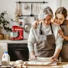An older woman and a younger woman are in a kitchen, baking together. The older woman is rolling out dough with a rolling pin, and the younger woman has her arms around her. Produktbild-Vorschau