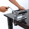 A person's hands operating a chrome pasta maker clamped to a dark wooden table. Anteprima dell’immagine prodotto