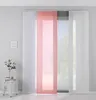 Panel curtains hanging in front of a window, with a small side table and plant to the left. Produktbild-Vorschau