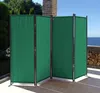 A green, four-panel room divider is set up on a patio with a view of the ocean. Produktbild-Vorschau