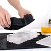 Hands are holding a black silicone ice cube mold over a tray of large ice cubes, with a glass of amber liquid and a lemon slice nearby. Náhled obrázku produktu