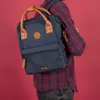A person wearing a plaid shirt is carrying a blue backpack with brown leather accents. Produktbild-Vorschau
