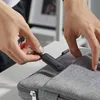 A person is placing a small black electronic device into a gray fabric bag. Anteprima dell’immagine prodotto