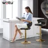 A woman sits on a bar stool reading a magazine in a modern kitchen or bar area. Produktbild-Vorschau