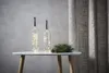 Two glass bottles with fairy lights inside, placed on a white table next to a pine branch and pine cone. A textured curtain is in the background. Produktbild-Vorschau