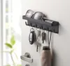 A black key holder with hooks is mounted on a wall next to a door handle. It holds several keys, sunglasses, and a small umbrella. Produktbild-Vorschau