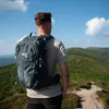 A person wearing a backpack stands on a mountain path, looking out at the landscape. Anteprima dell’immagine prodotto