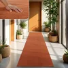 A long orange rug is laid out in a hallway with potted plants and wooden doors. Produktbild-Vorschau