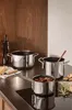 A kitchen counter with several stainless steel pots and pans, along with some ingredients like cheese and rosemary. Náhled obrázku produktu