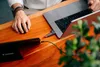 A person's hands using a laptop, mouse, and external hard drive on a wooden desk. Náhľad obrázku produktu