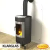 A modern black wood-burning stove with a glass door, installed against a white wall with a metal heat shield behind it. The stove is on a wooden floor. Produktbild-Vorschau