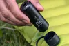 A hand holding a black electric pump over a yellow air mattress outdoors. Podgląd zdjęcia produktu