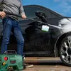A person is washing a black car with a pressure washer. Produktbild-Vorschau