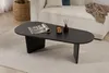 A black oval coffee table with a magazine, candle, and diffuser on it, placed on a light gray rug in a living room setting. Voir les images du produit