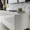A close-up view of a modern white high-gloss TV cabinet with gold legs, decorated with a gold bear figurine and books. Náhľad obrázku produktu