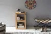 A room interior with a wooden shelf unit, a clock on the wall, and a bench with boots. Produktbild-Vorschau