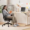 A woman is sitting in an ergonomic office chair and reading a book next to a standing desk. Anteprima dell’immagine prodotto