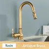 A close-up shot of an antique brass kitchen faucet with a pull-out spray head, set against a light blue wall and a stainless steel sink. Náhled obrázku produktu