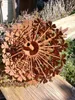 A rusty metal garden decoration shaped like a dandelion or flower, with clover-like petals, sits on a wooden surface outdoors. Anteprima dell’immagine prodotto