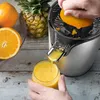 A person is using an electric juicer to make orange juice, with a pineapple and oranges in the background. Produktbild-Vorschau