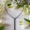 A black metal heart-shaped garden stake is placed in front of white flowers and greenery on a white wooden surface. Produktbild-Vorschau