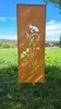 A decorative metal panel with a floral design stands in a grassy outdoor setting. Produktbild-Vorschau