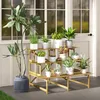 A tiered wooden plant stand filled with various potted plants is placed on a patio in front of a white-paneled wall with windows. Produktbild-Vorschau