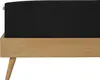 A close-up side view of a black mattress on a wooden bed frame with angled legs. Produktbild-Vorschau