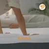 A person's hands are pressing into a mattress, demonstrating its softness and support. The Emma logo is visible on the mattress. Produktbild-Vorschau