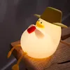 A glowing duck-shaped night light with a hat sits on a wooden surface. Produktbild-Vorschau