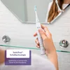 A person is holding a white electric toothbrush in front of a bathroom mirror. Produktbild-Vorschau