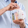 A person is holding a clear plastic container filled with small packets. Náhľad obrázku produktu