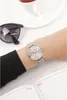 A person's wrist wearing a watch, with sunglasses and a cup of tea in the background, and an open notebook in the foreground. Produktbild-Vorschau