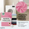 A folded pink fitted sheet is shown in the foreground, with a stack of other colored fitted sheets behind it. A washing machine is visible in the background. A close-up of pink fabric is in the upper right corner. Produktbild-Vorschau
