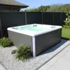 An outdoor hot tub is set up in a garden with a fence and landscaping. Podgląd zdjęcia produktu