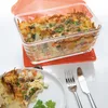 A casserole dish filled with food, with a portion served on a plate, accompanied by cutlery. Produktbild-Vorschau
