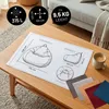 A diagram of a beanbag chair with dimensions and capacity, along with fabric swatches, is laid out on a wooden coffee table. Produktbild-Vorschau