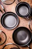 A collection of professional-grade cookware, including frying pans and pots, arranged on a wooden surface. Náhled obrázku produktu