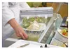 A person in a white lab coat is wrapping a sandwich with plastic wrap using a dispenser. Náhľad obrázku produktu