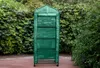 A green greenhouse with shelves stands outdoors against a backdrop of lush green foliage. Anteprima dell’immagine prodotto