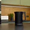 A black electric kettle is placed on a dark countertop in a modern kitchen setting. Anteprima dell’immagine prodotto